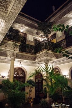 an indoor courtyard at night with potted plants and hanging lights on the balconies