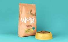 a bag of waggy dog food next to a yellow bowl on a blue background