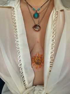 a woman with tattoos on her chest wearing a white shirt and holding a blue necklace