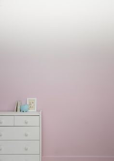 a white dresser sitting next to a pink wall in a child's room with a teddy bear on top