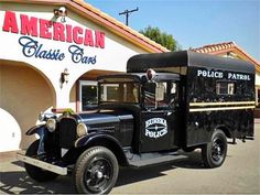 an old black truck parked in front of a building with american classic cars written on it