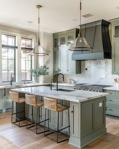 a kitchen with green cabinets and white marble counter tops, two pendant lights hanging over the island