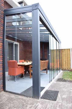 an outdoor dining area with glass walls and sliding doors on the side of a brick building