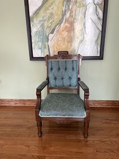 a blue chair sitting in front of a painting on the wall next to a wooden floor