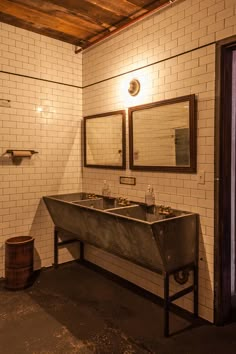 a bathroom with two sinks and mirrors on the wall, in front of a brick wall