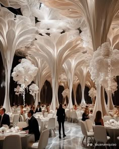 people are sitting at tables in the middle of a room with tall white trees on either side