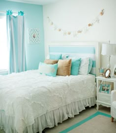 a bed room with a neatly made bed next to a window and a sky blue wall