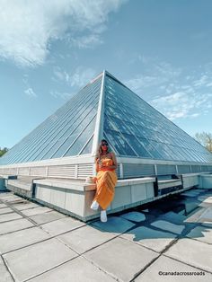 a woman sitting on the edge of a building looking at her cell phone while wearing an orange outfit