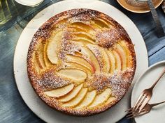 an apple cake with powdered sugar on top sits on a table next to other desserts