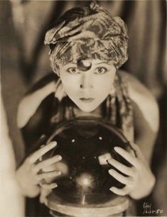 an old photo of a woman holding a ball in front of her face and looking at the camera