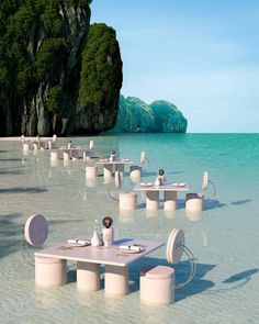 tables and chairs are set up in the shallow water near an island with green trees