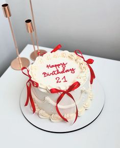 a white birthday cake with red ribbon and candles