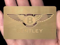 a hand holding a gold business card with the bentley logo on it's front