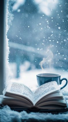 an open book and cup of coffee sit on a snowy window sill