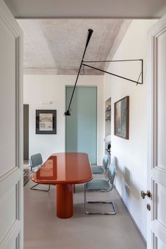 an orange table in the middle of a room with chairs and pictures on the wall