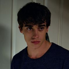 a young man is staring at the camera while wearing a blue shirt and standing in front of a white door