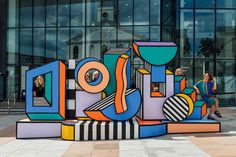 a woman walking past a large colorful sign in front of a building