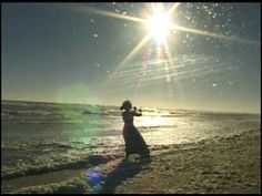 a woman standing on top of a sandy beach next to the ocean under a bright sun