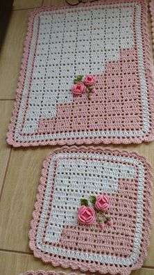 two crocheted placemats with pink roses on them sitting on the floor