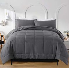 a bed with grey comforter and pillows in a room