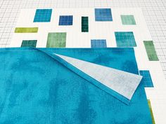 a piece of fabric is laying on top of a quilted tablecloth with squares and rectangles