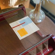 a close up of a weaving machine on a table with a vase in the background