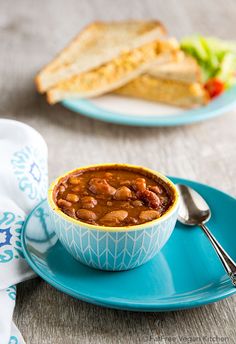 a blue plate topped with a bowl of chili next to a sandwich on a white and blue plate