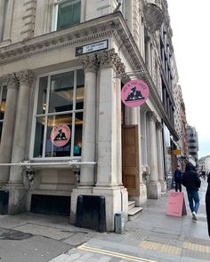 people are walking down the sidewalk in front of a building with pink signs on it