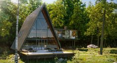 a triangular shaped house in the woods surrounded by tall trees and grass, with two people standing outside