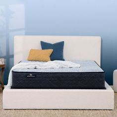 a bed with blue and yellow pillows on top of it next to a white couch