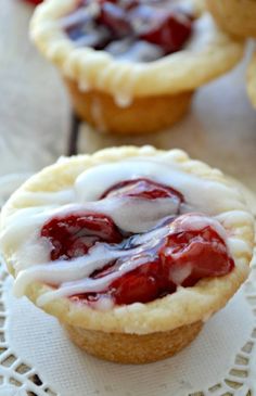 small pies with icing and strawberries are on a doily