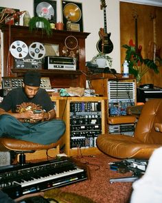 a man sitting on top of a brown chair in front of a musical equipment collection