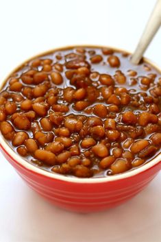 a red bowl filled with baked beans on top of a white table next to a spoon