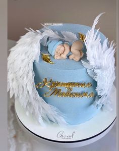 a baby is sleeping on top of a blue cake with white feathers and gold lettering