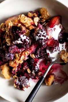 a white bowl filled with fruit and granola on top of a table next to a spoon