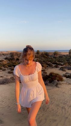 a woman in white dress walking on the beach