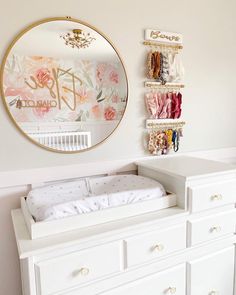 a baby crib in front of a round mirror and wall hanging on the wall