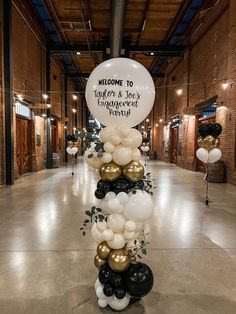 a welcome sign with balloons and greenery in the middle of an indoor space that is decorated with gold, white and black