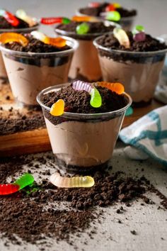 four cups filled with dirt sitting on top of a wooden table covered in dirt and candy