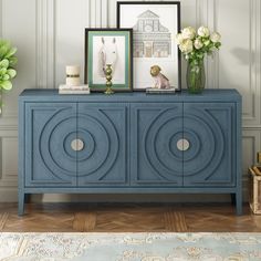 a blue sideboard with two pictures on top and flowers in vases next to it