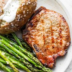 grilled steak and asparagus on a white plate with a bagel bun