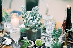 the table is set with succulents, candles and silverware on it