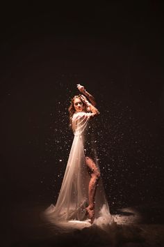 a woman in a white dress is dancing with water splashing on her face and body