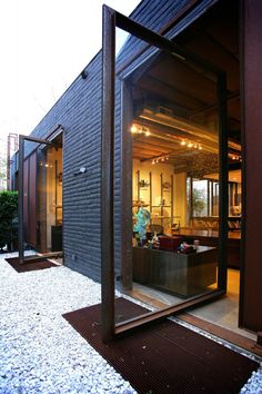 an open door leading into a room with glass walls and doors on the outside, in front of a black building