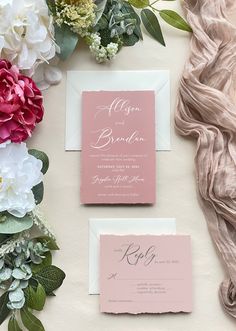 the wedding stationery is laid out with flowers and greenery on top of it