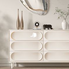 a white dresser with an oval mirror above it and vases on the top shelf