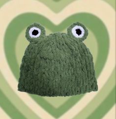 a green knitted hat with two eyes and a heart shaped pattern in the background