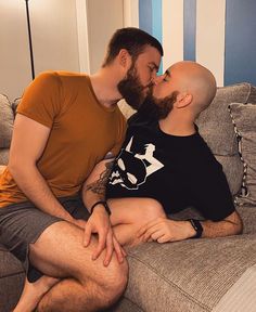 two men are sitting on a couch and one is kissing the other's cheek