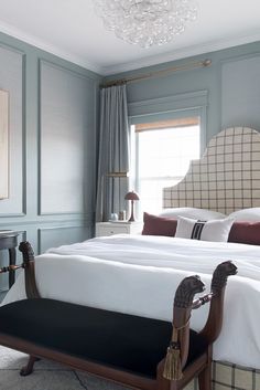 a bedroom with blue walls, white bedding and a chandelier hanging from the ceiling