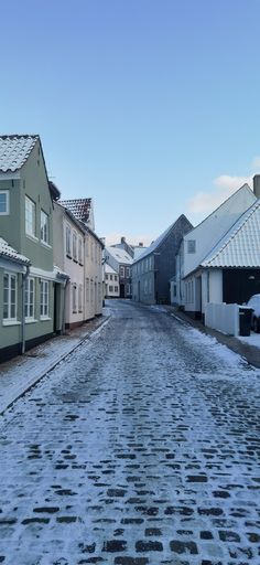 an empty street with snow on the ground and houses in the background, during winter